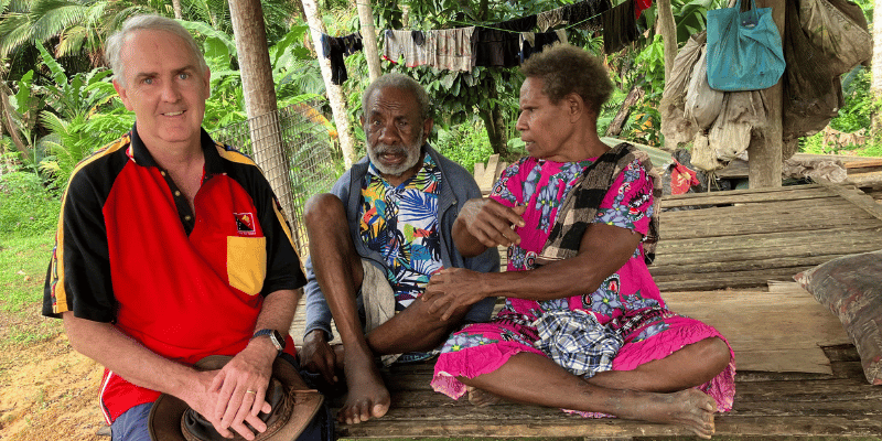 Dr Daniel Priest sitting with local villagers in Papua New Guinea